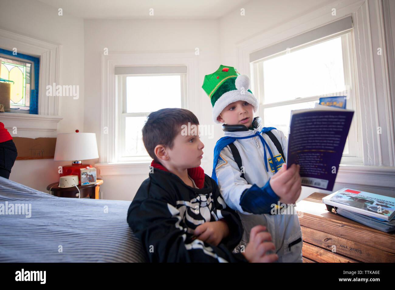 Brothers reading book in brightly lit bedroom Stock Photo