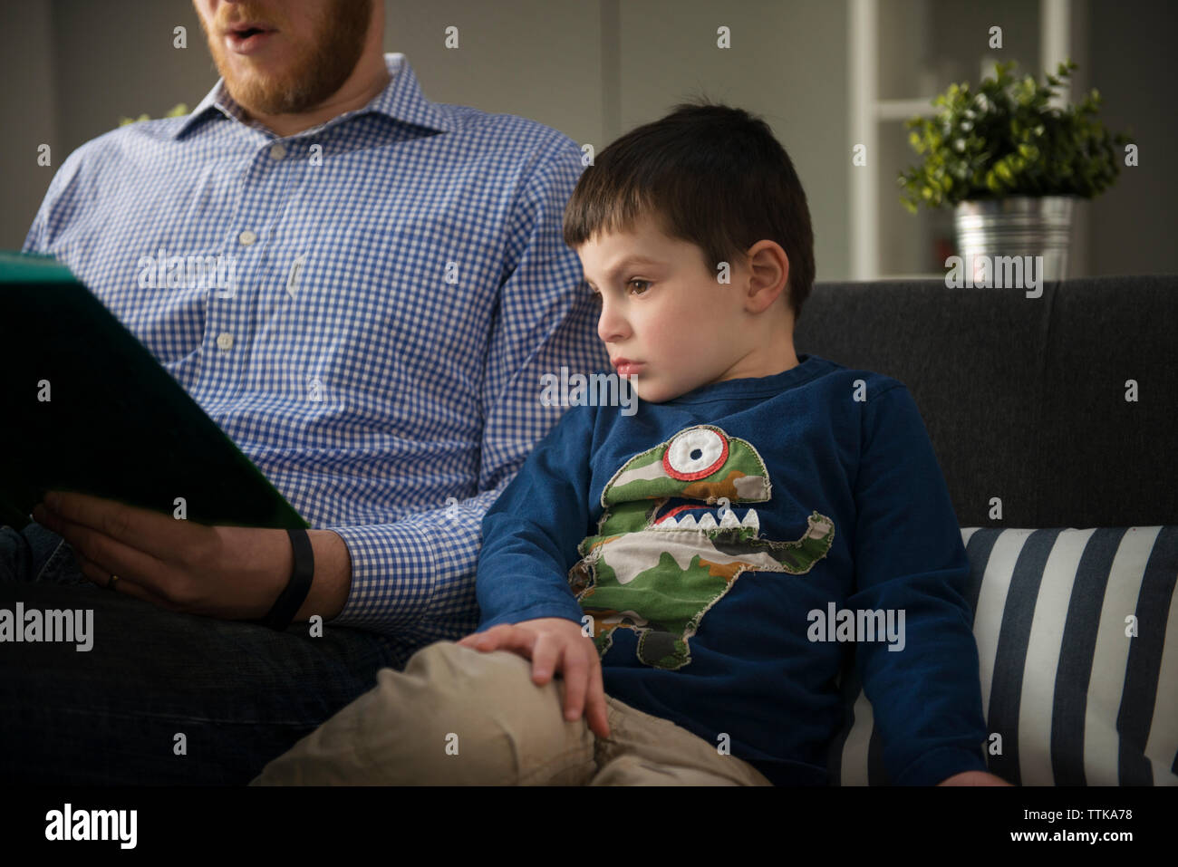 Boy looking at book while sitting with father on sofa Stock Photo