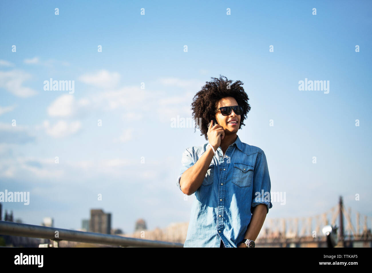 Young man talking on phone while standing against cityscape Stock Photo
