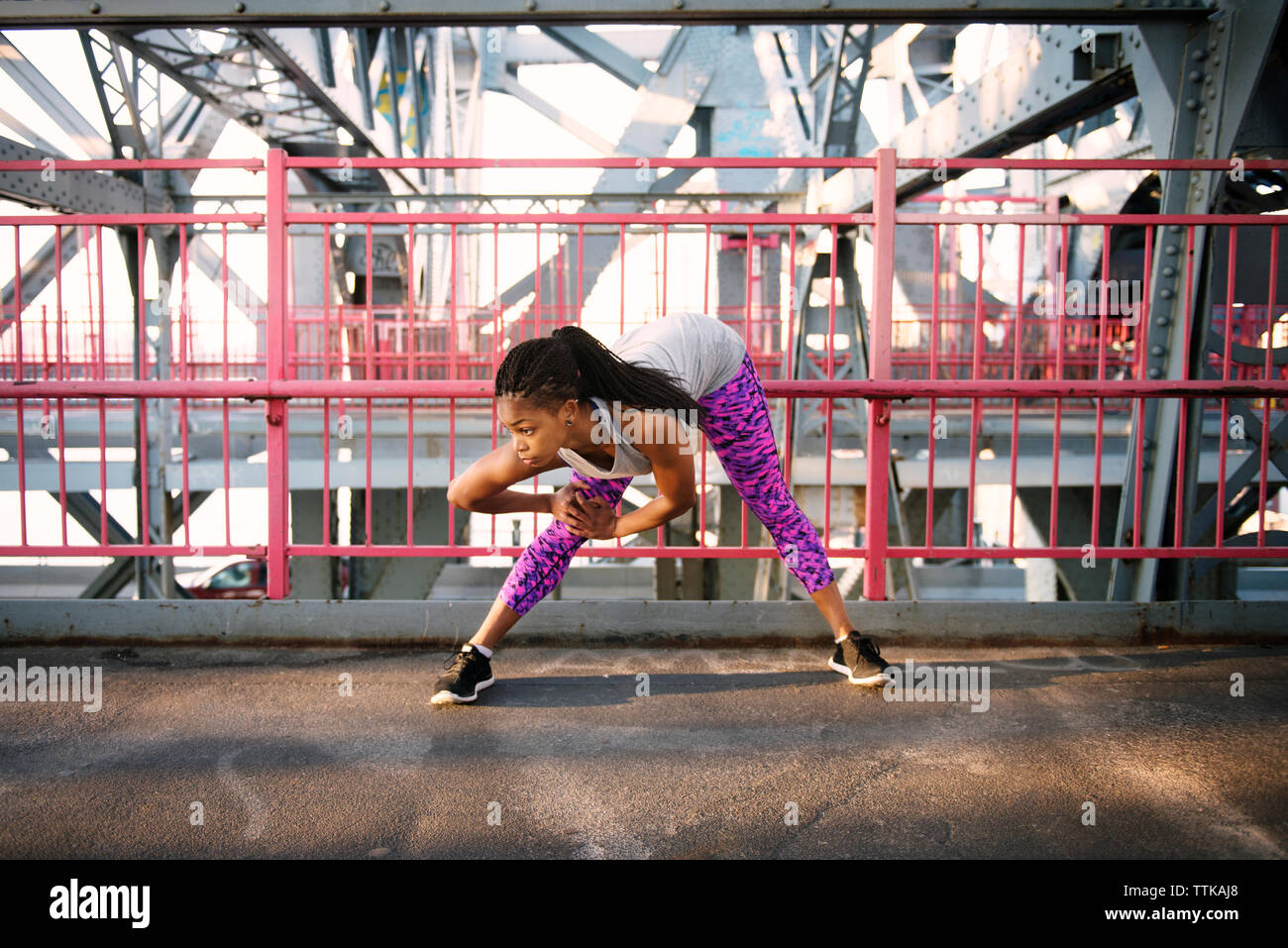 Woman stretching while exercising on bridge in city Stock Photo