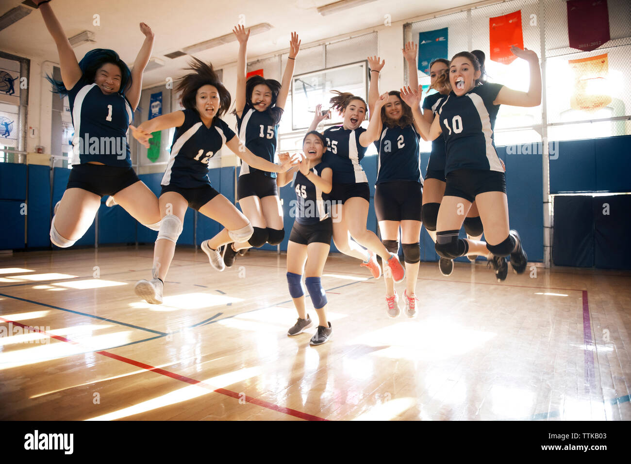Happy female volleyball team jumping at court Stock Photo