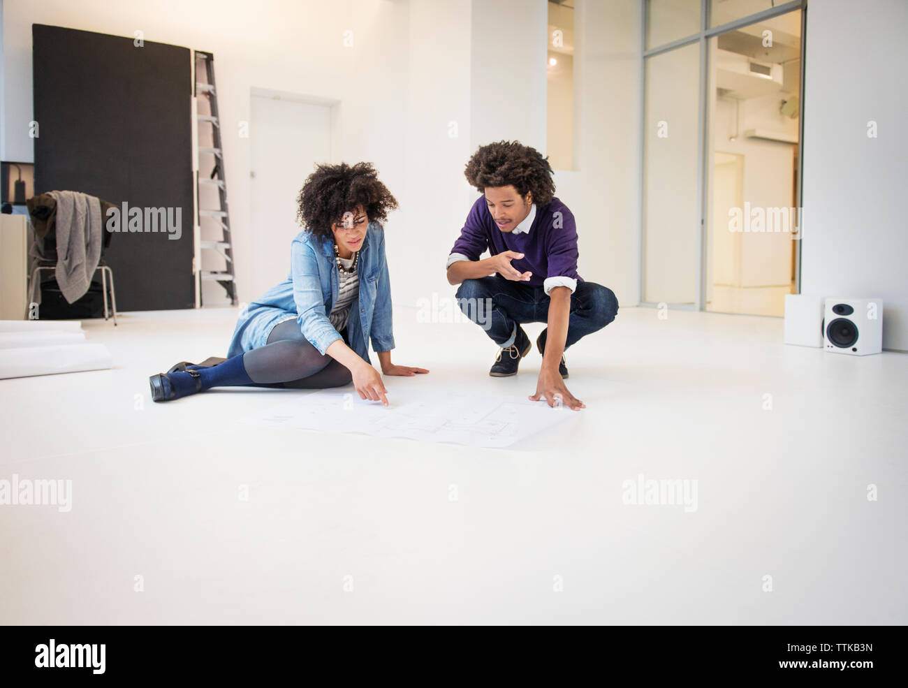 Young business colleagues discussing over chart while sitting on floor in creative office Stock Photo