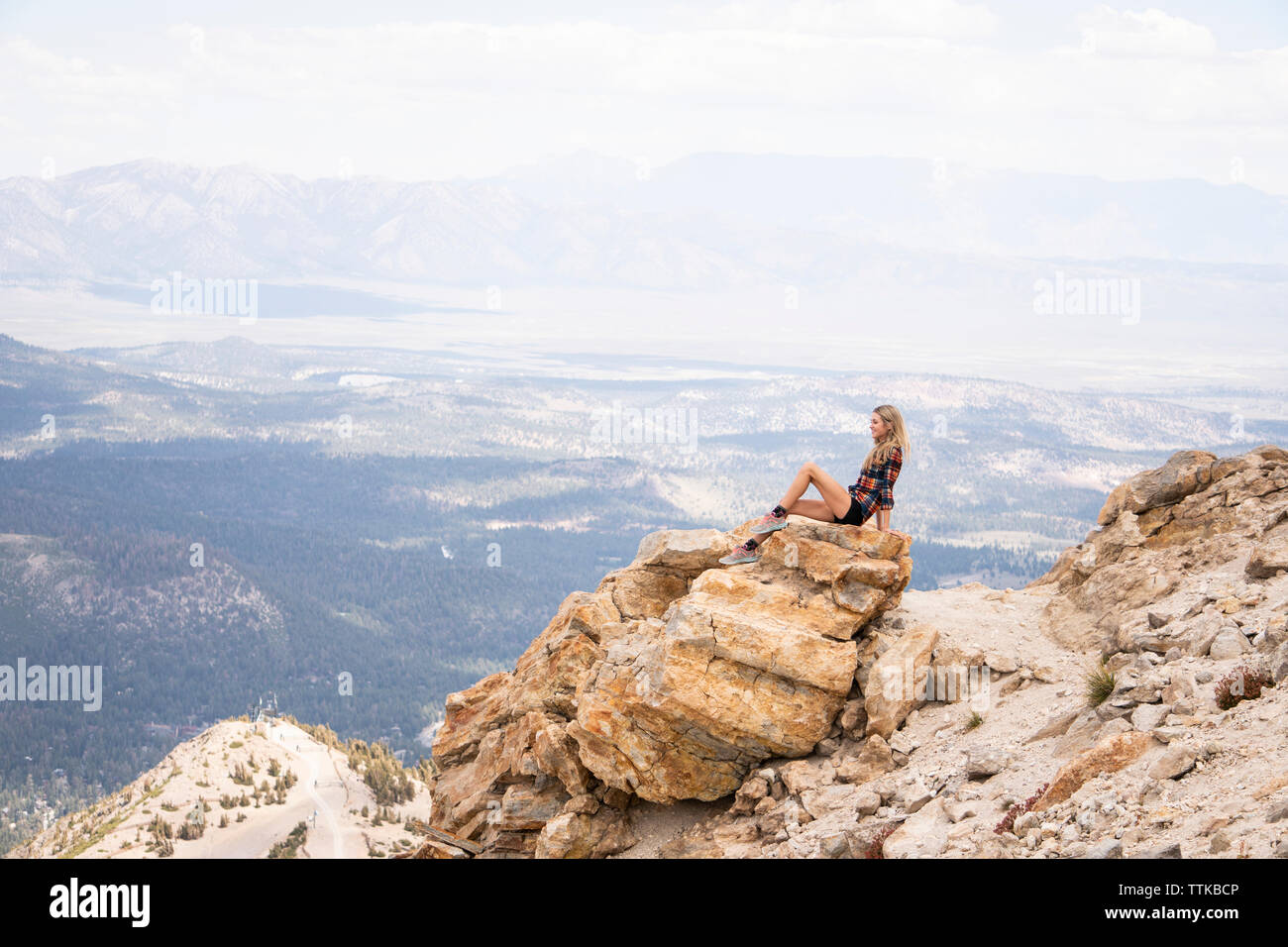 Side view of female tourist looking at landscape while sitting on rock against cloudy sky Stock Photo