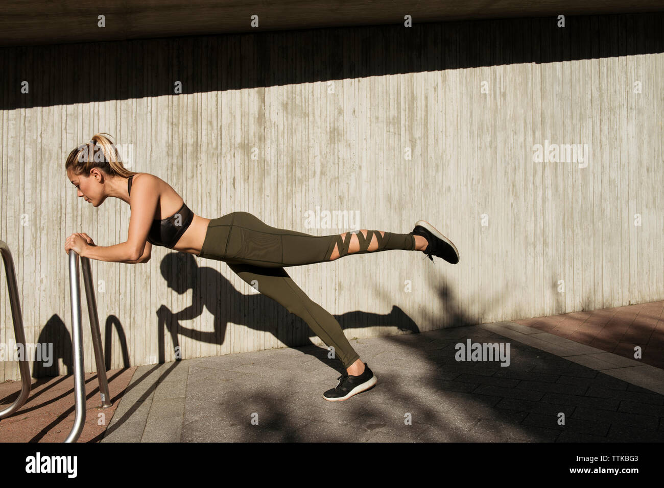 Side view of young woman exercising on metal against wall Stock Photo ...