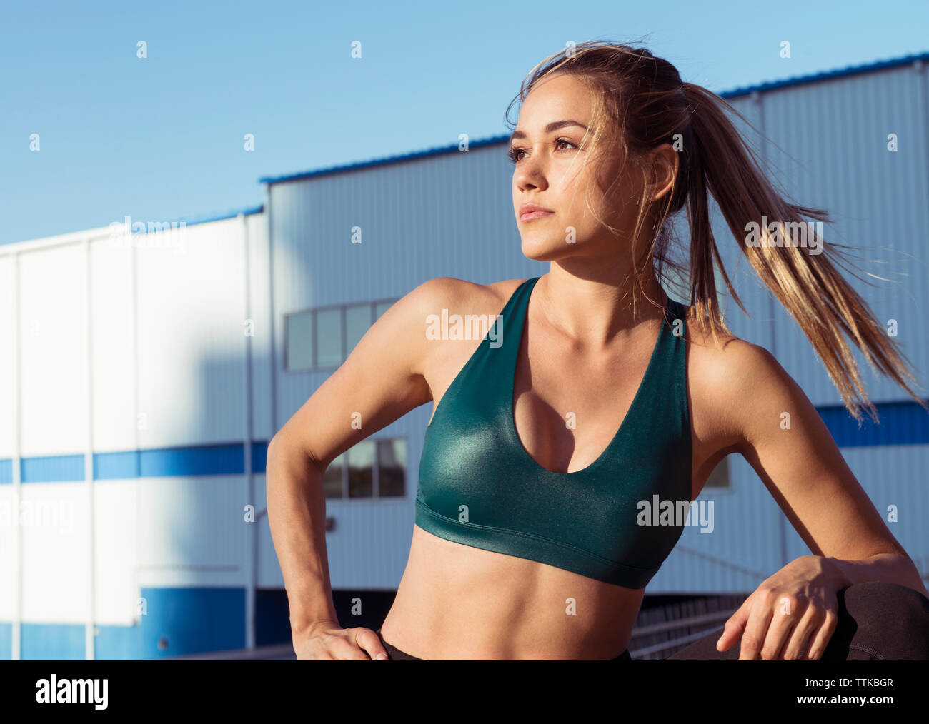 Thoughtful young woman wearing sports bra while standing against