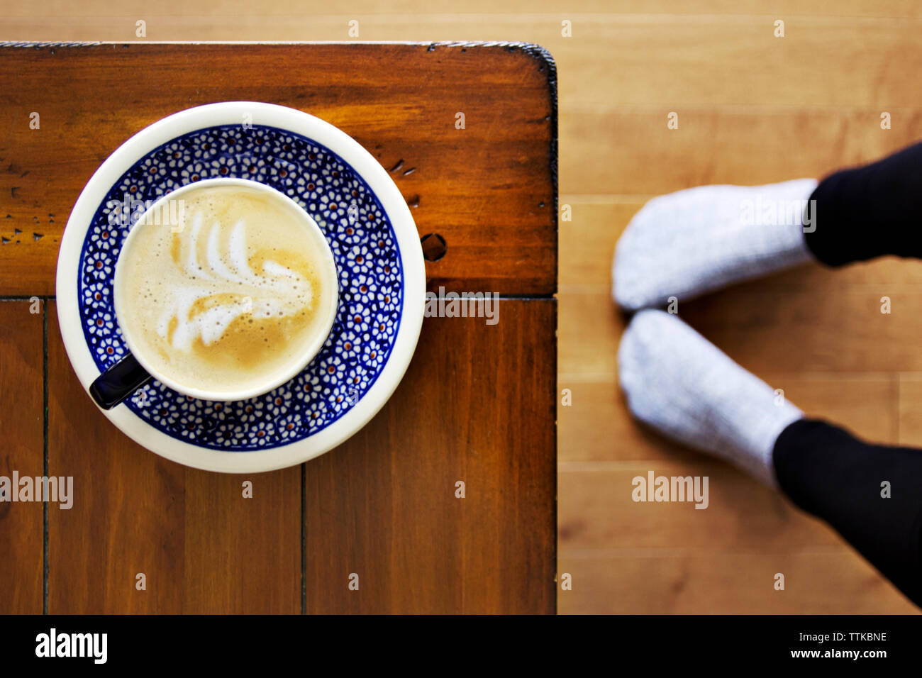 Overhead view of cappuccino served on wooden table by woman's legs Stock Photo