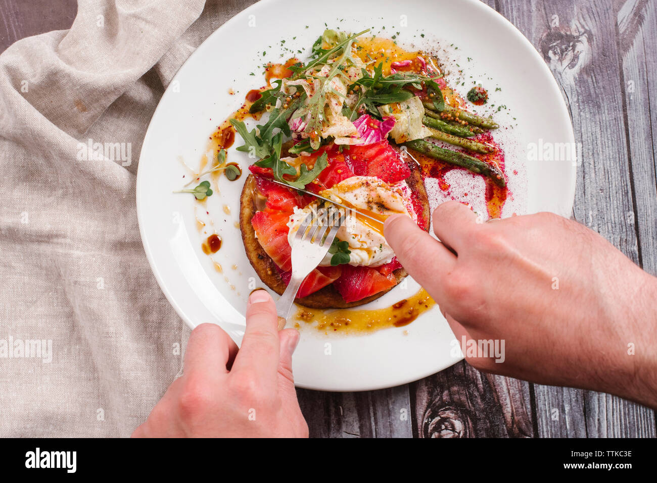 Cropped hands of man having savory crepes with salmon and poached egg in plate on table Stock Photo
