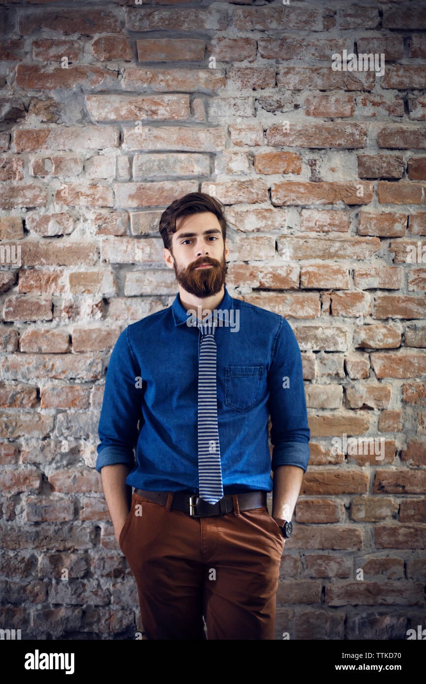 Portrait of confident businessman standing against brick wall in office Stock Photo