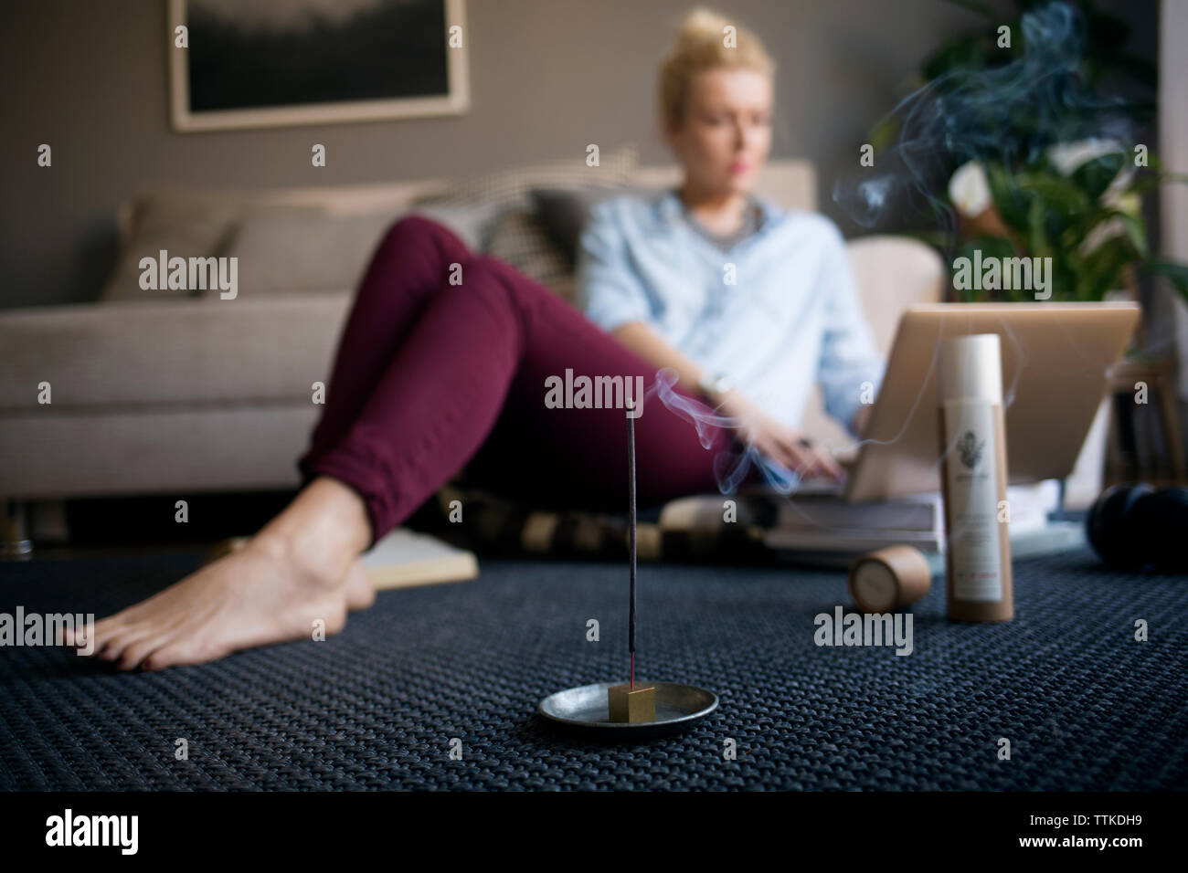 Smoke coming out from incense stick on floor with woman working in background Stock Photo