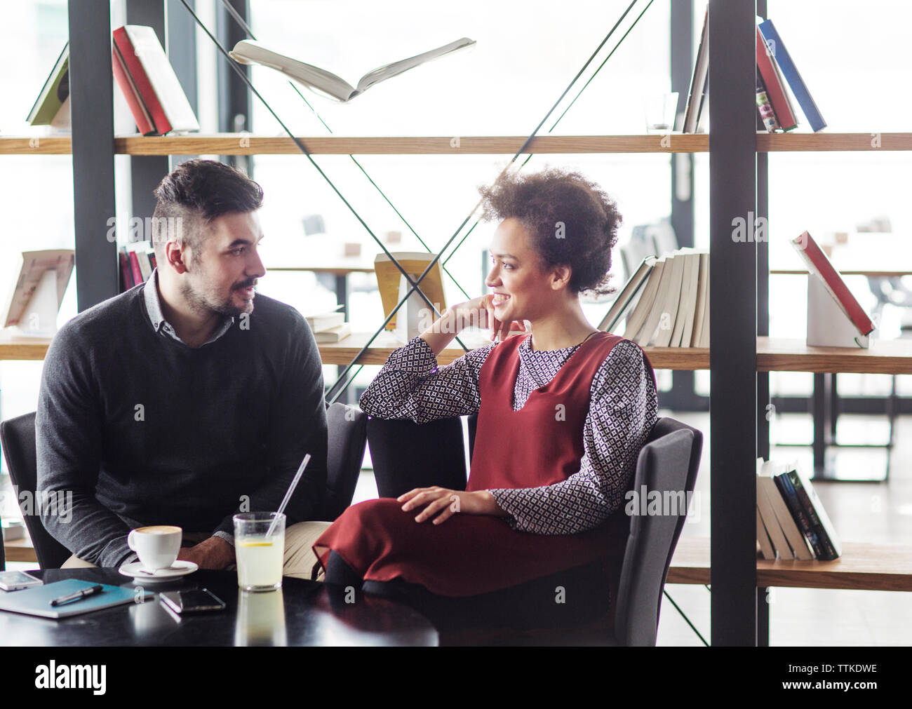 business couple talking while sitting at table against book shelf in restaurant Stock Photo