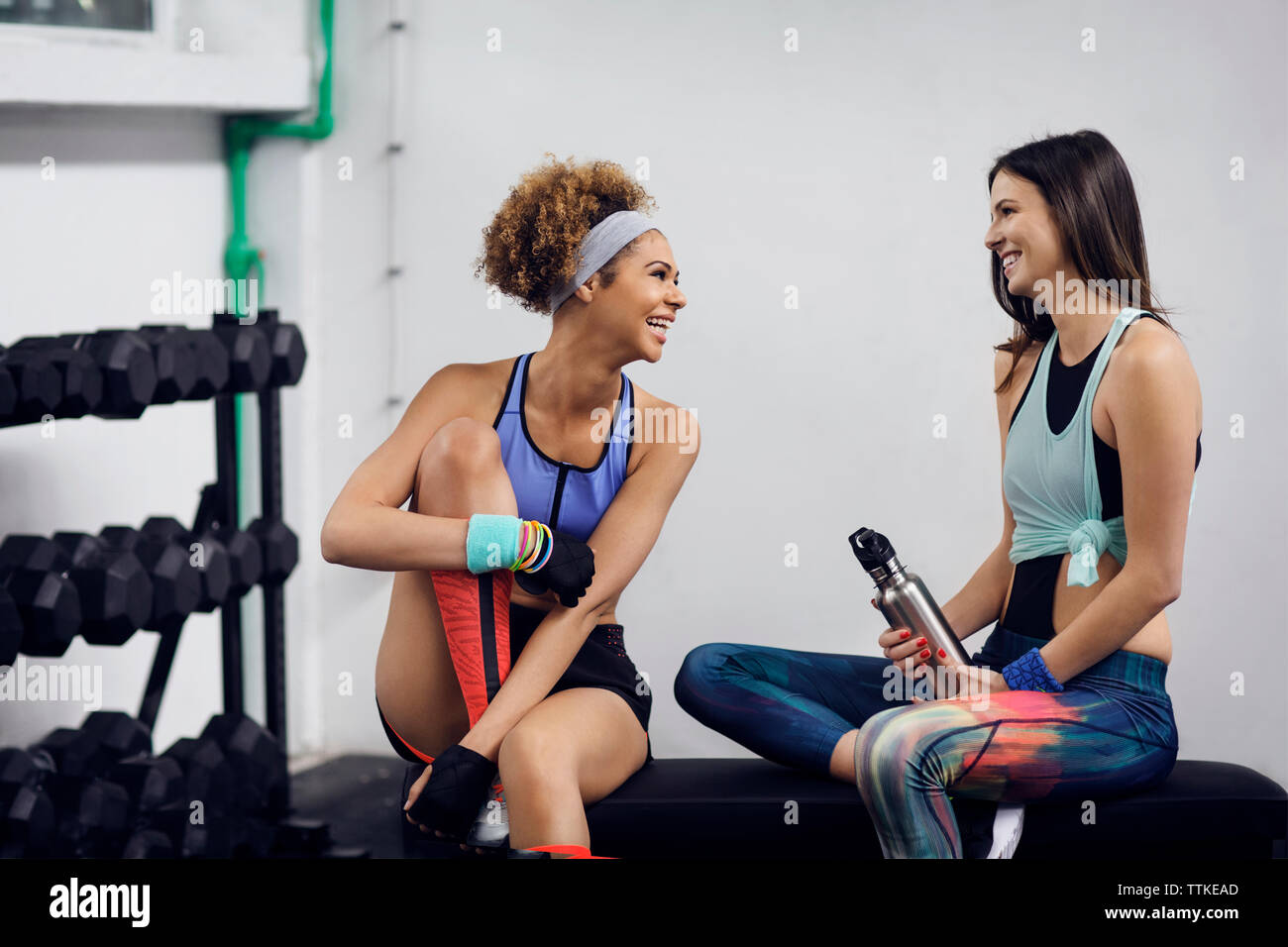Happy female athletes talking while sitting on bench at gym Stock Photo