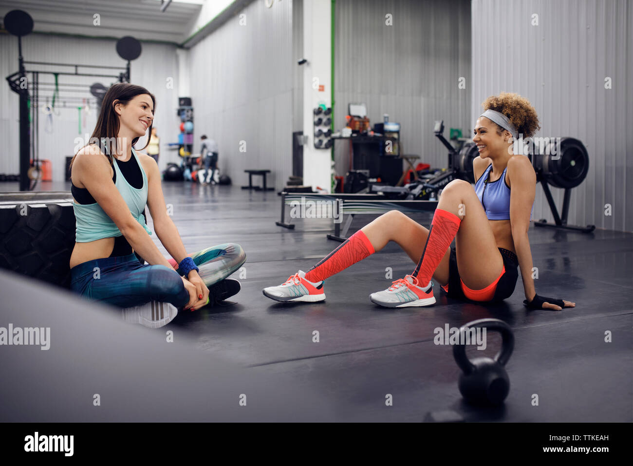 Happy female athletes talking while sitting on floor at gym Stock Photo