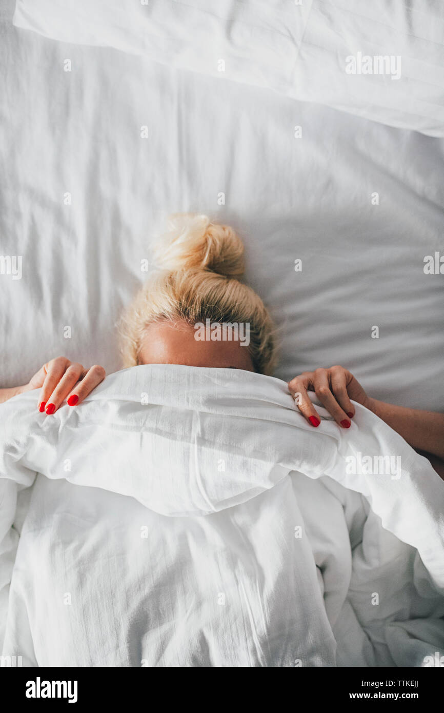 Overhead view of woman covering face with blanket on bed Stock Photo