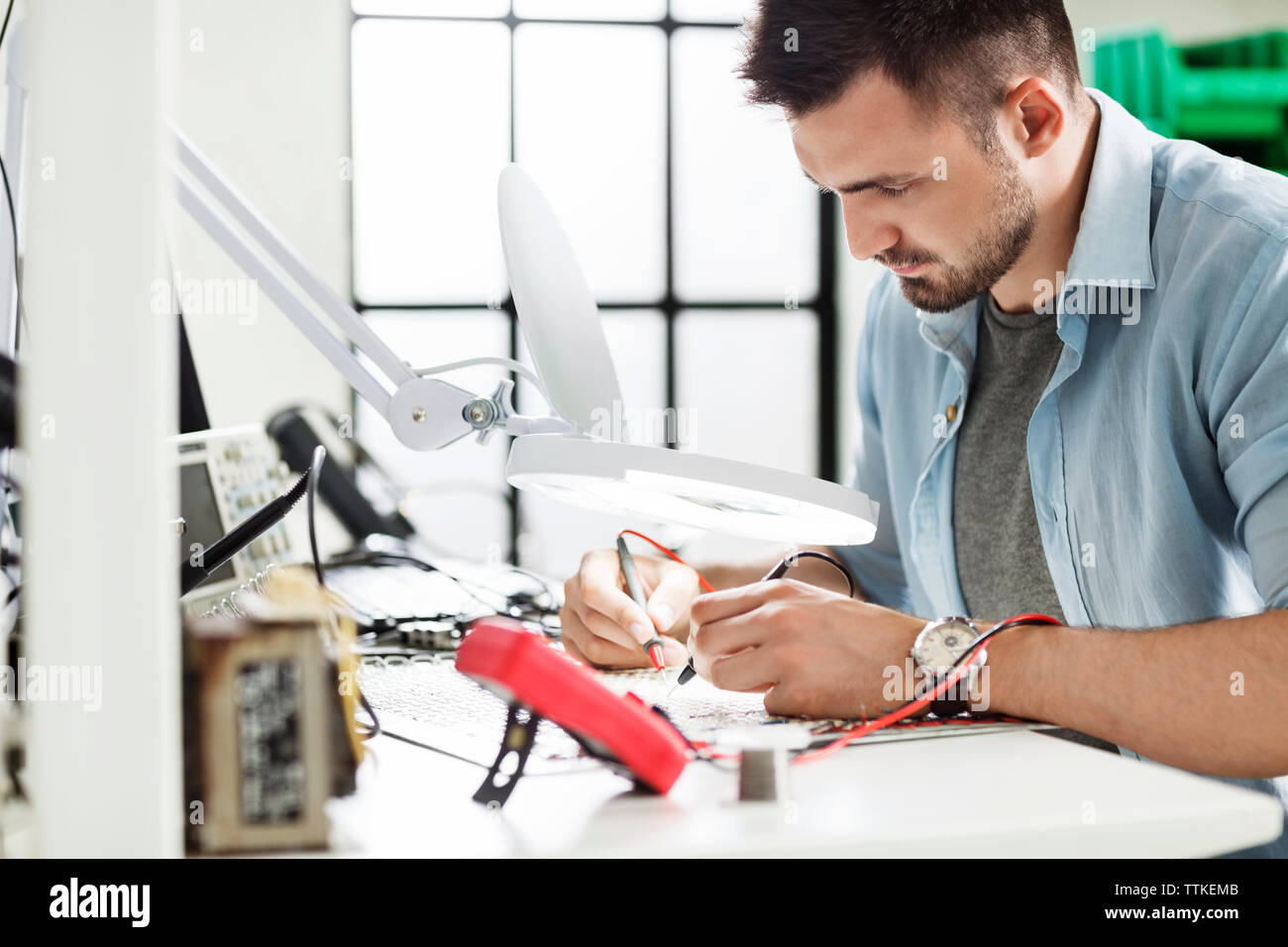 Concentrated engineer soldering circuit at table in electronics