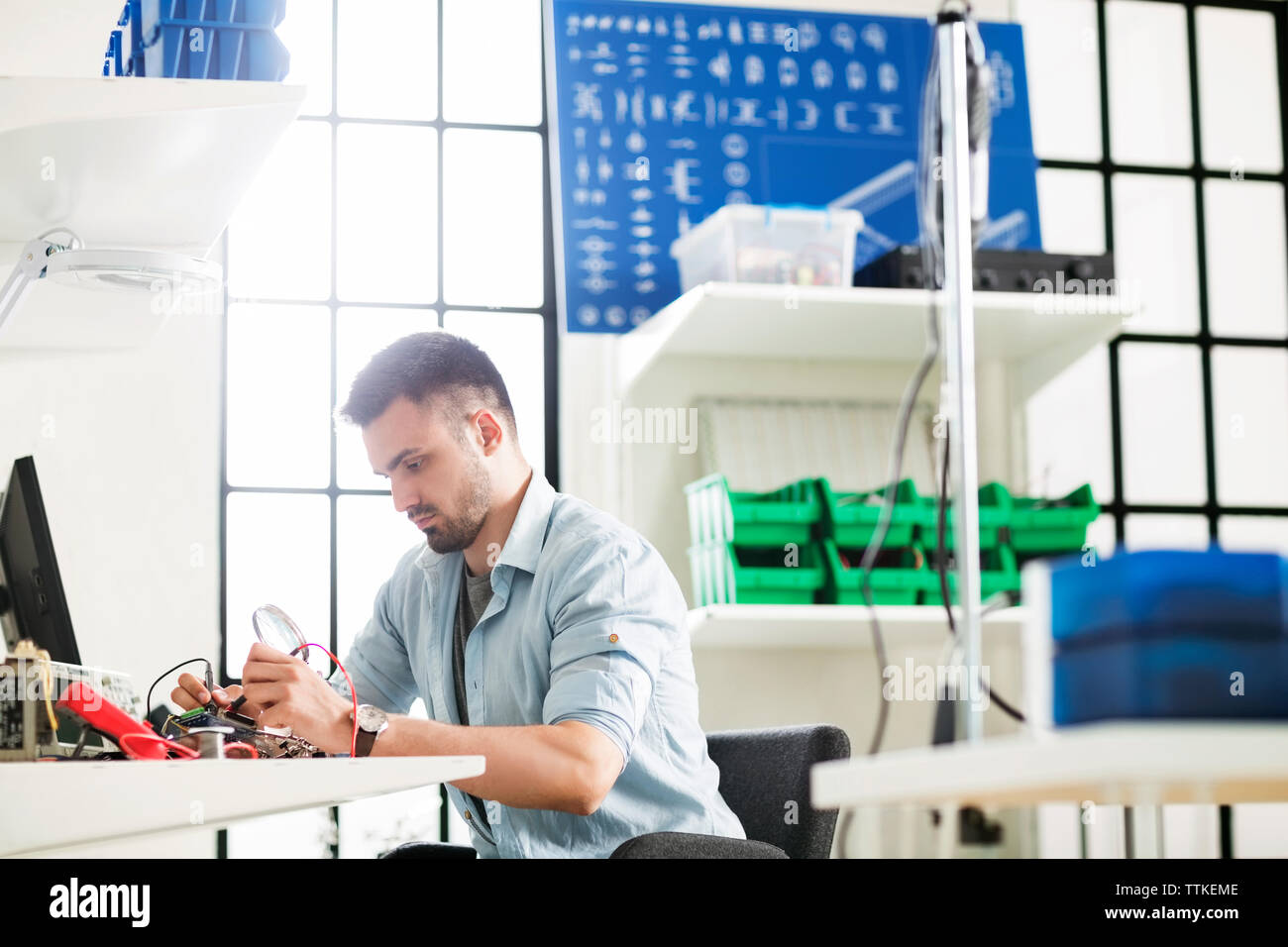 Serious engineer working on circuit board at table in electronics industry Stock Photo