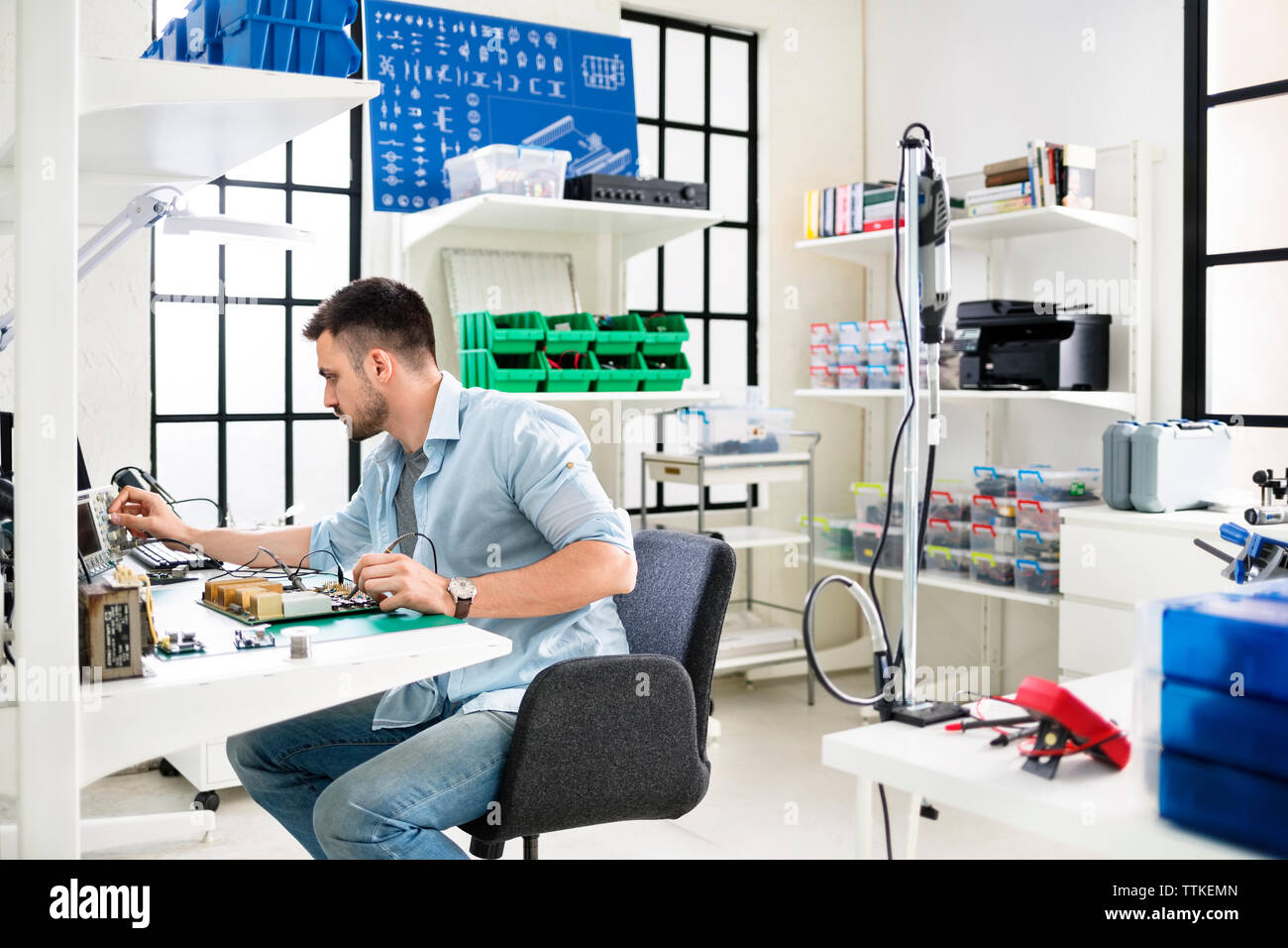 Serious technician working on circuit board at table in electronics industry Stock Photo