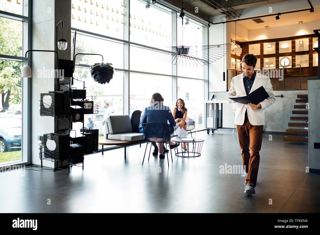 businessman reading file while walking in office by colleagues in background Stock Photo