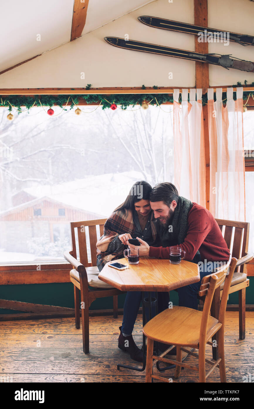 Couple using mobile phone while sitting by window in cafe Stock Photo