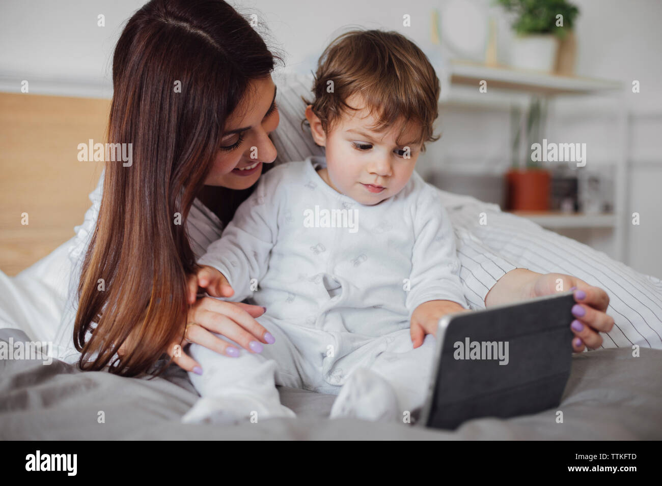 Happy mother using tablet computer with baby boy on bed Stock Photo