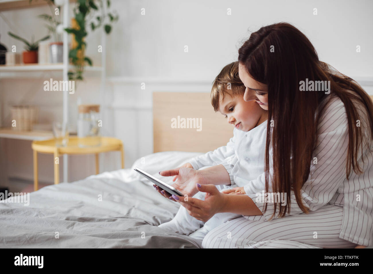 Mother and baby boy using tablet computer while sitting on bed Stock Photo