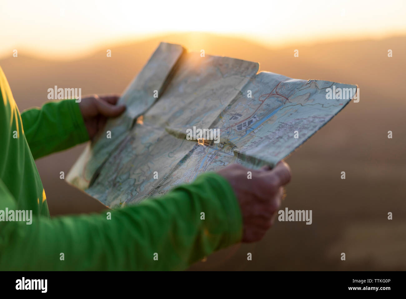 Close up of senior male hands holding a map on top of mountain during sunset Stock Photo