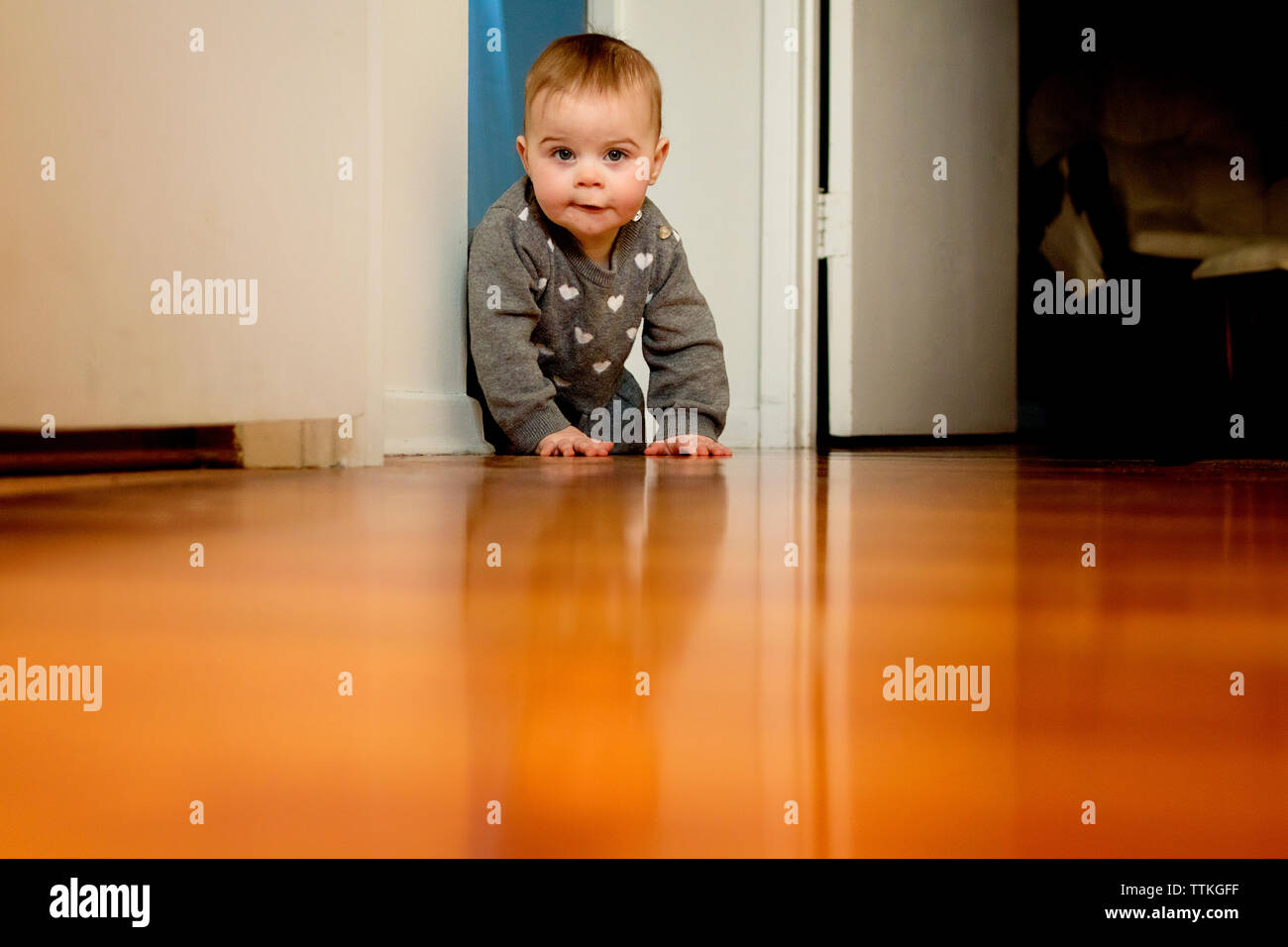 A baby girl crawling on the floor past a door way Stock Photo