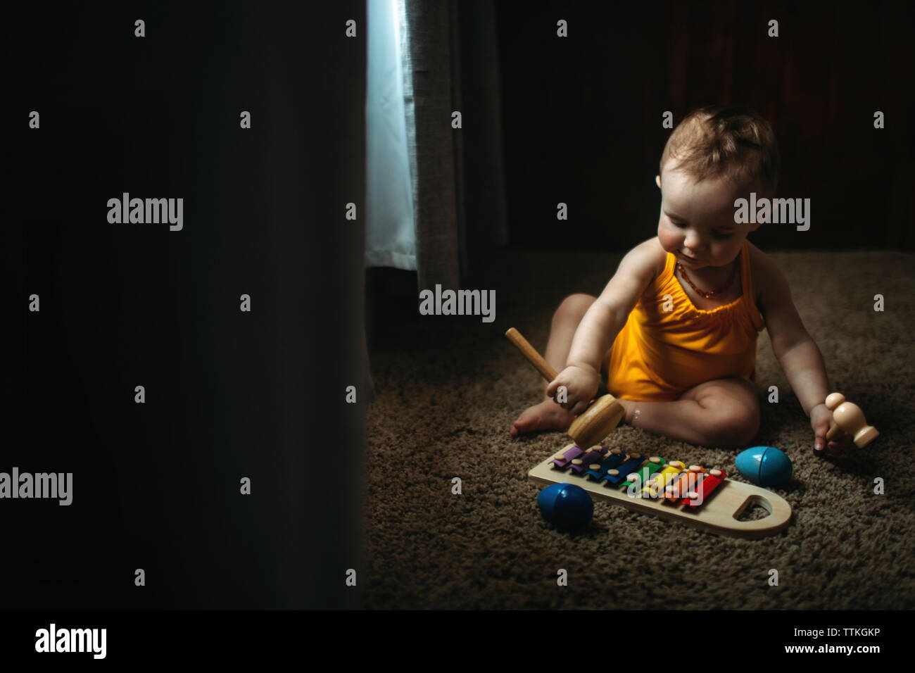 Baby girl playing xylophone on rug at home Stock Photo