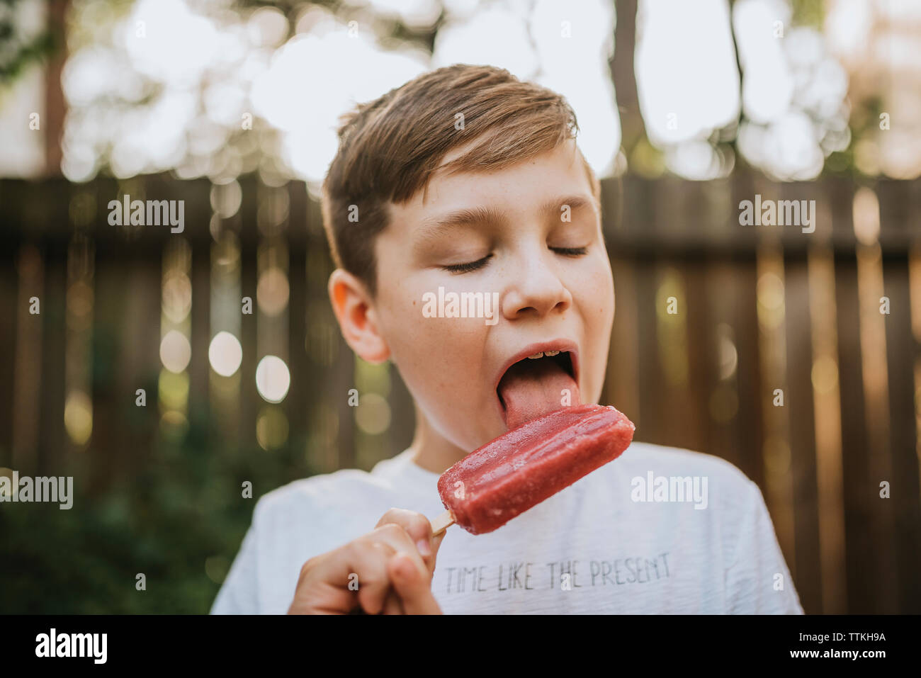 Close-up of boy licking popsicle at backyard during summer Stock Photo