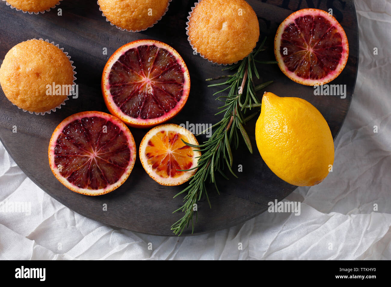 High angle view of fairy cakes with rosemary and citrus fruits on cutting board Stock Photo