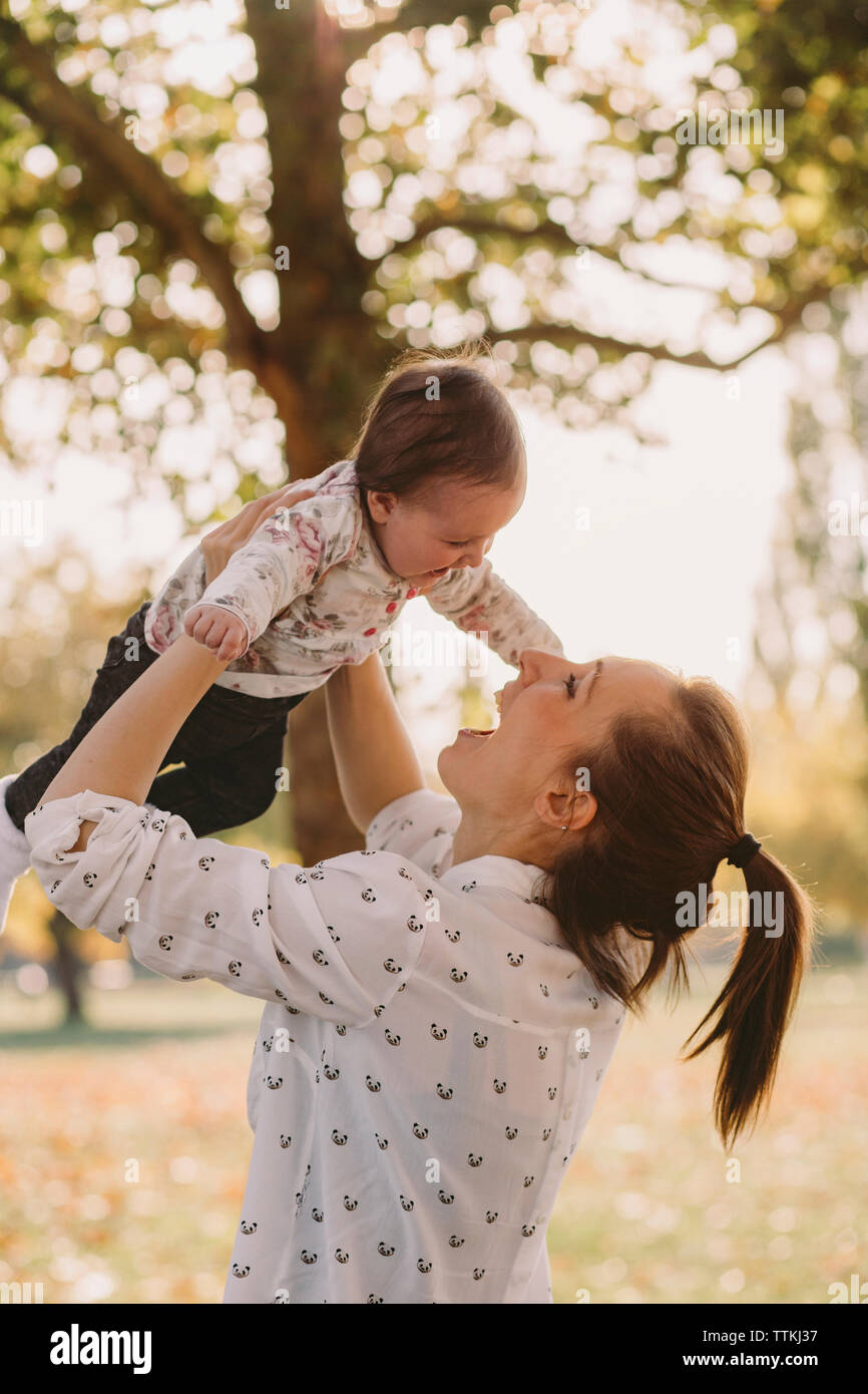 Happy mother picking up cute daughter while standing at park during autumn Stock Photo