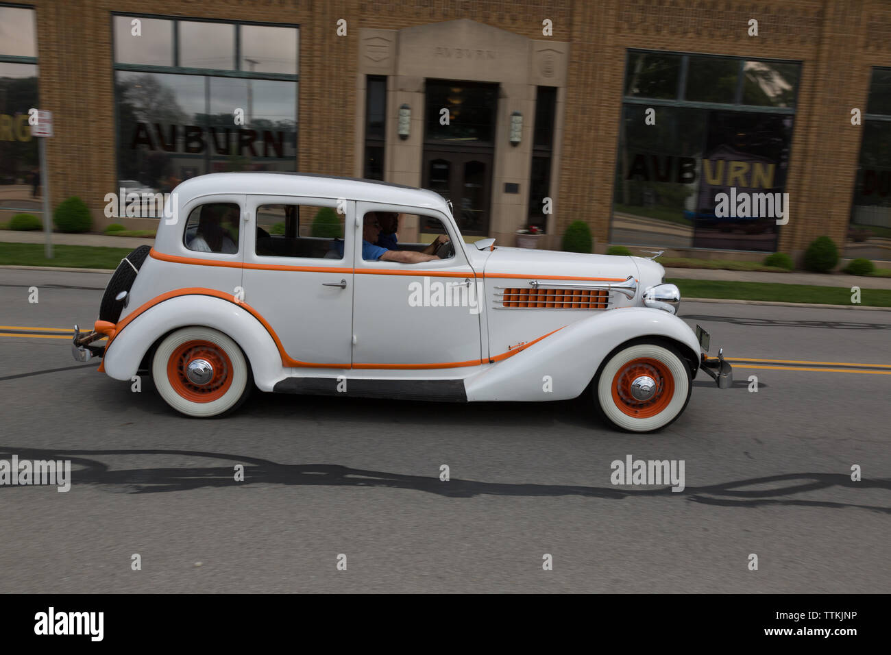 An antique 1935 Auburn 653 sedan passes by the Auburn Cord Duesenberg Museum (the original Auburn Automobile Company building) in Auburn, Indiana, USA. Stock Photo