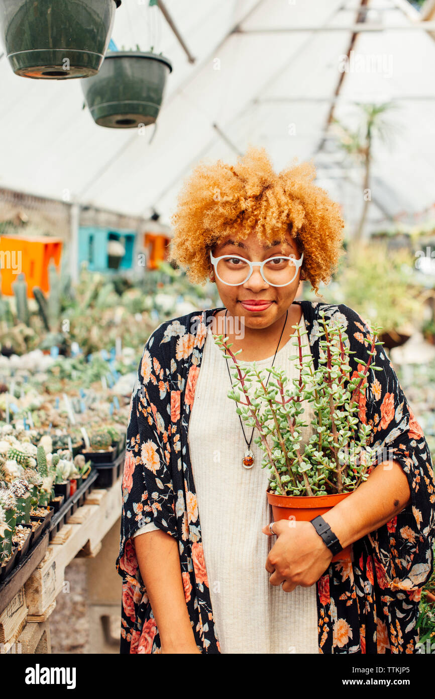 Portrait of woman holding potted plant while standing in nursery Stock ...