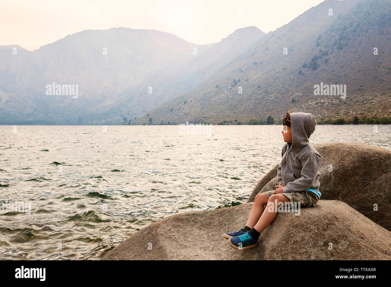 Boy sitting on rock by Convict Lake against mountains Stock Photo - Alamy