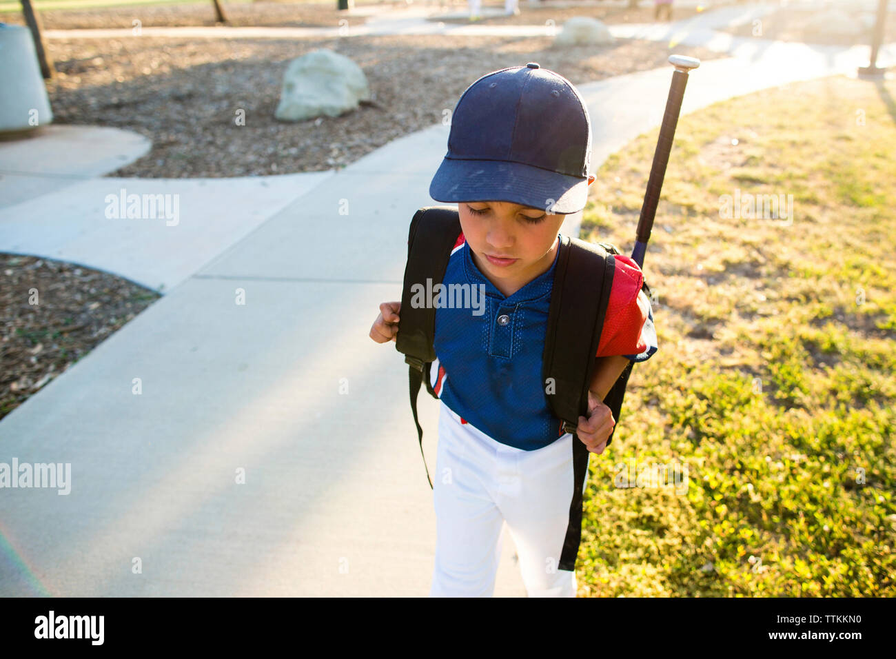 High angle view of boy in baseball uniform with backpack walking in yard Stock Photo