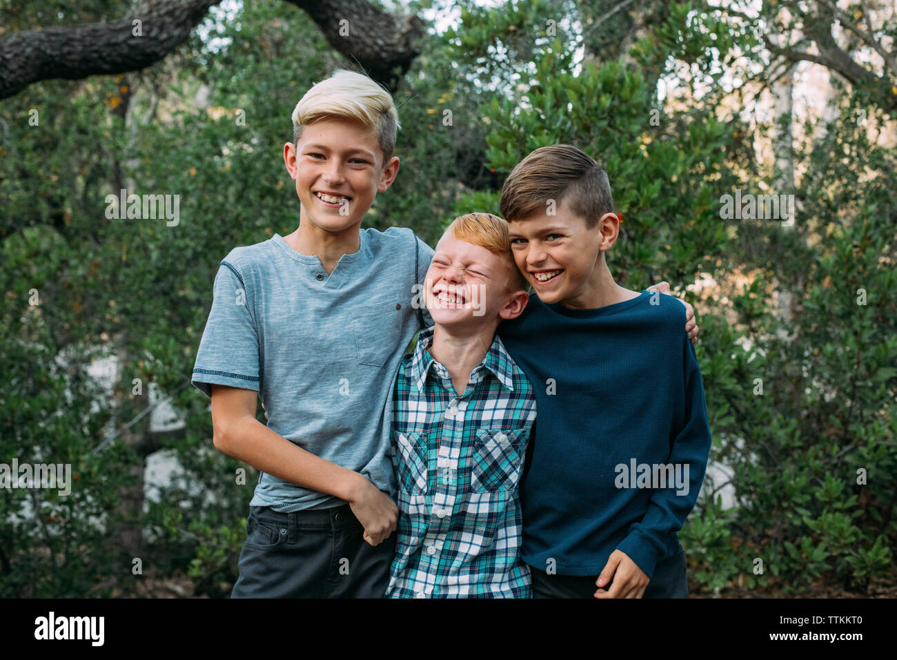 Happy brothers standing side by side against trees at park Stock Photo
