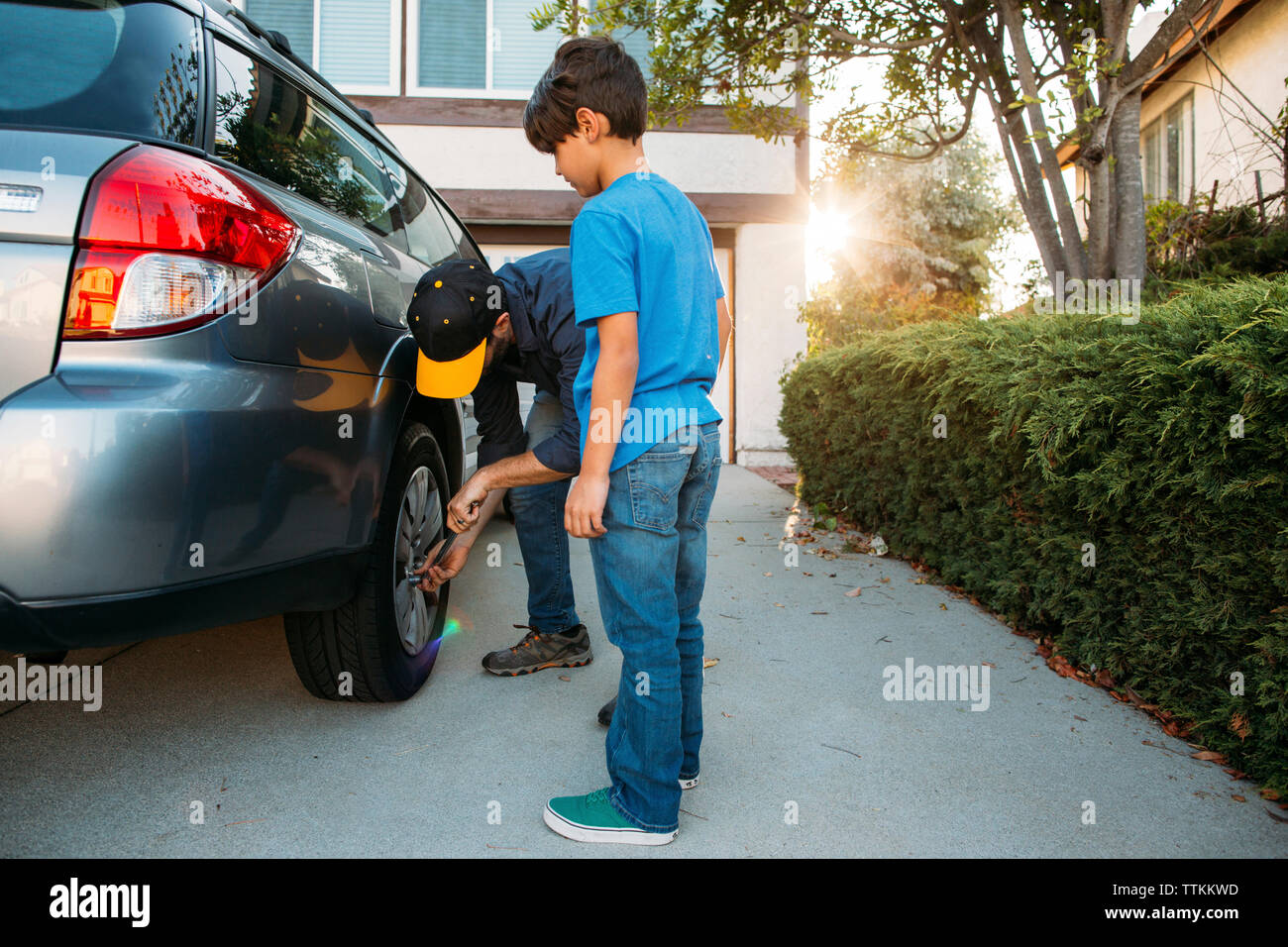 Son looking at father tightening tire with spanner at driveway Stock Photo