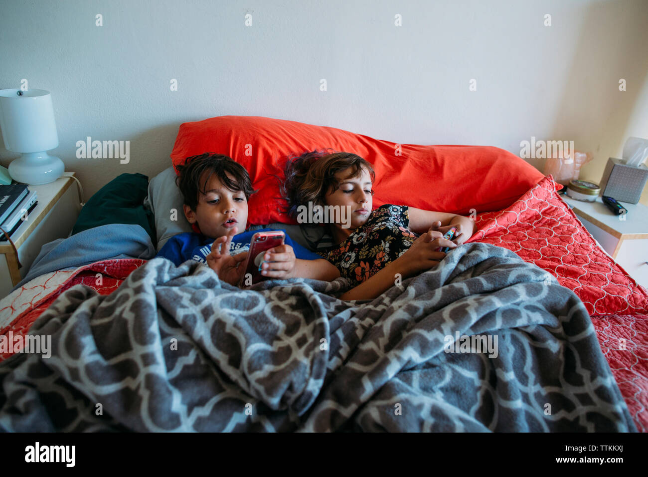 High angle view of siblings using smart phones while lying on bed Stock Photo
