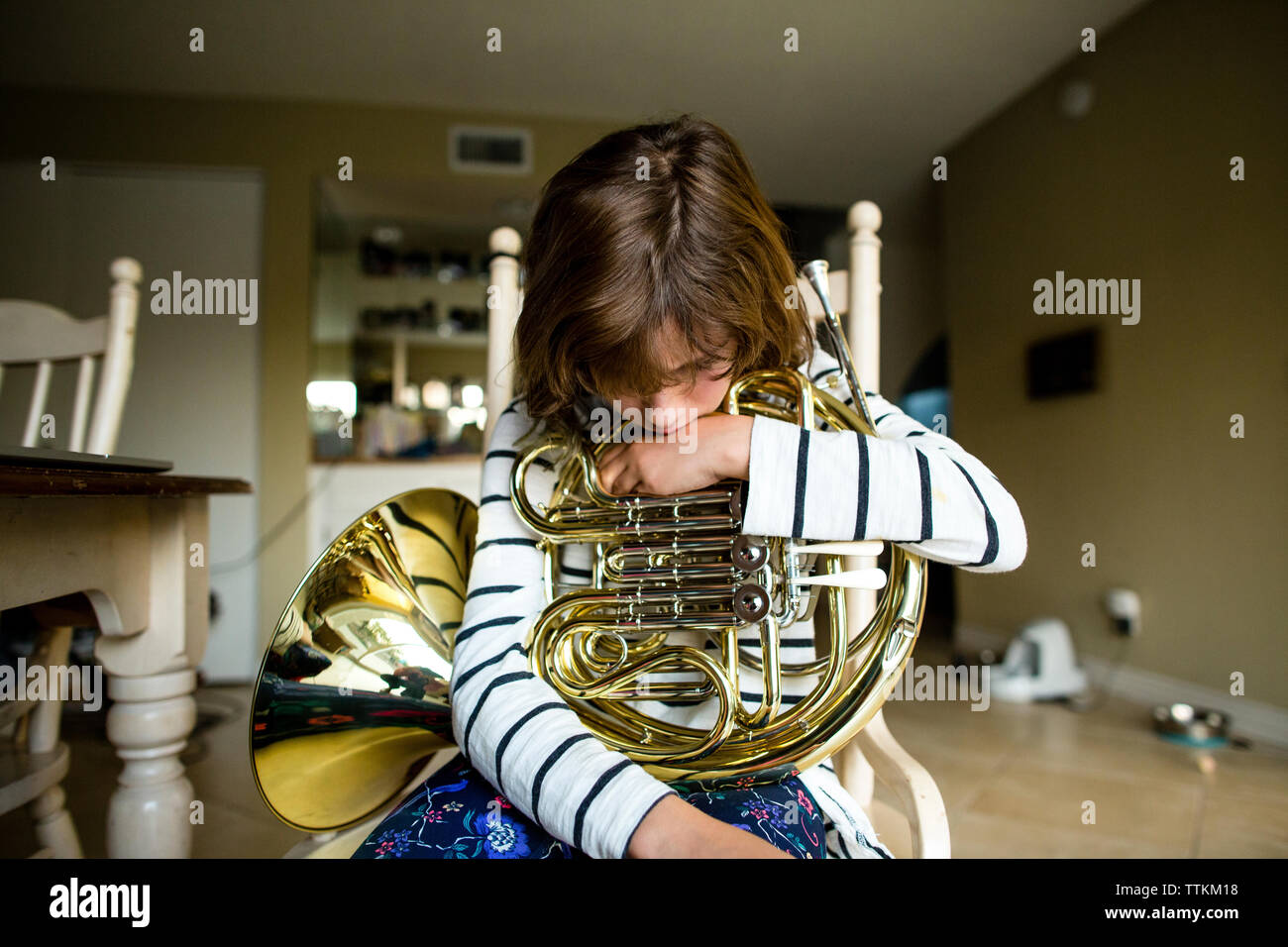 Girl with French horn sitting on chair at home Stock Photo