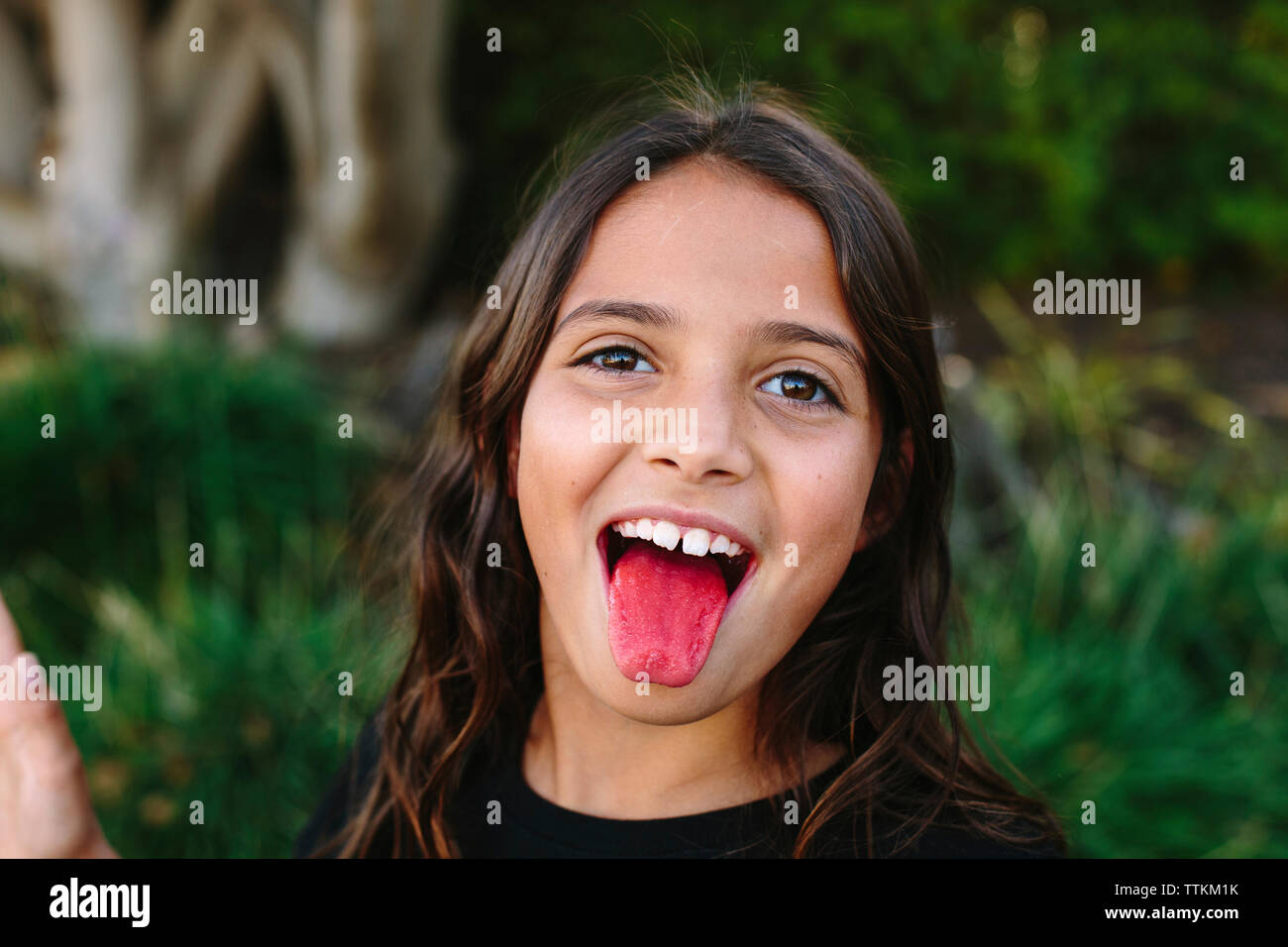 Close-up portrait of girl sticking out tongue at park Stock Photo