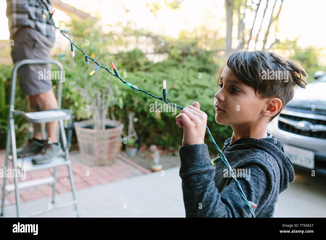 Son assisting father in hanging colorful string lights during christmas Stock Photo