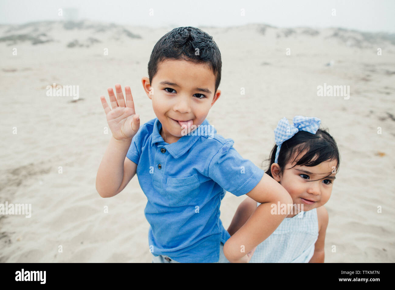 Little Boy Poses Silly With Tongue Out With Sister Looking Off Stock Photo