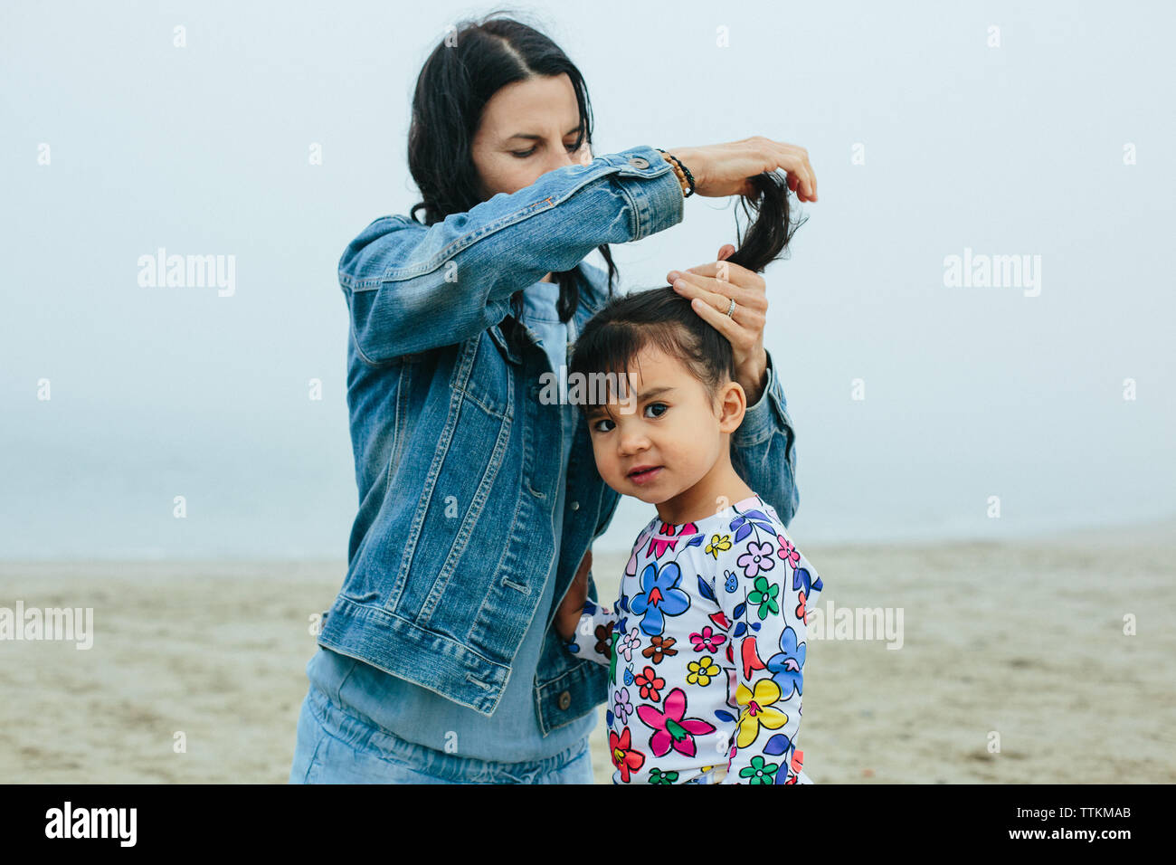 Mother Puts Toddler Daughter's Hair In a Pig Tail At Beach Stock Photo