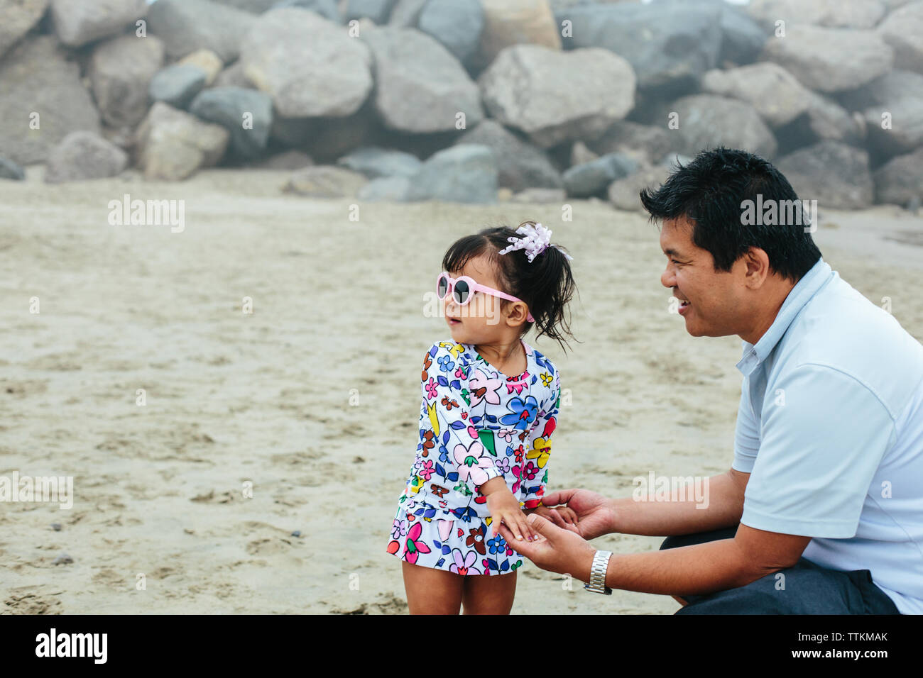 Father Smiles At Daughter While Holding Hands At Beach Stock Photo