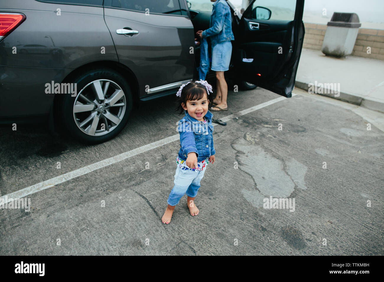 Toddler Girl Pointing And Looking At Camera In Parking Lot Stock Photo