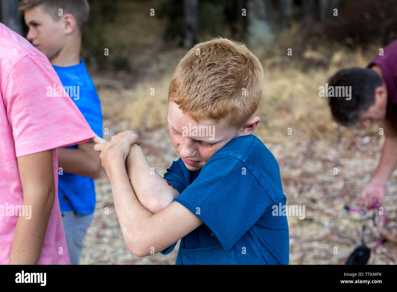 Boy with red hair and freckles observes the scrape on his arm Stock Photo