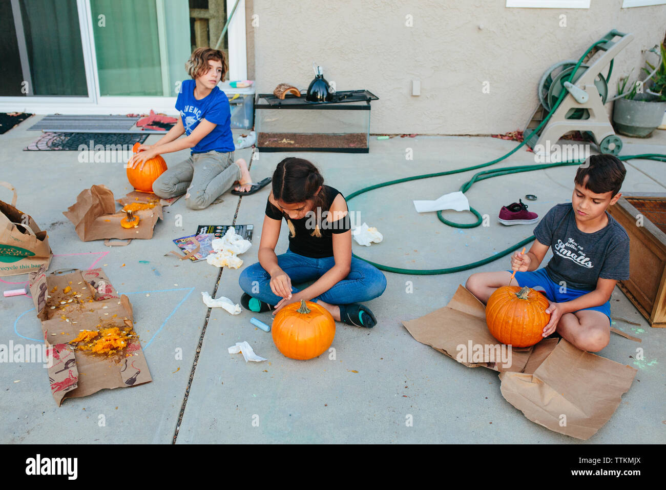 Three siblings carve pumpkins together outside Stock Photo