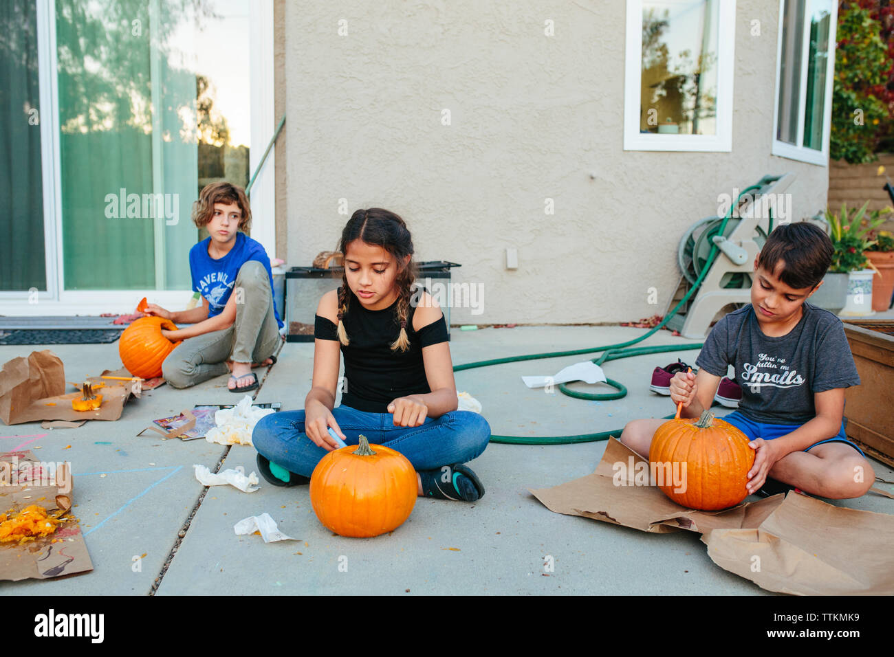 Two sisters and brother carve pumpkins outside Stock Photo - Alamy
