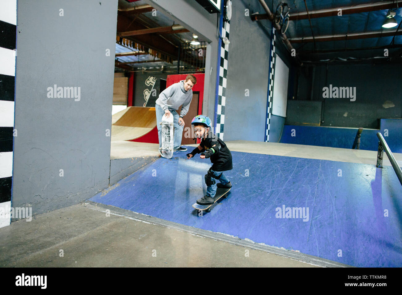 Little boy skates down a ramp while instructor stands behind to watch Stock Photo