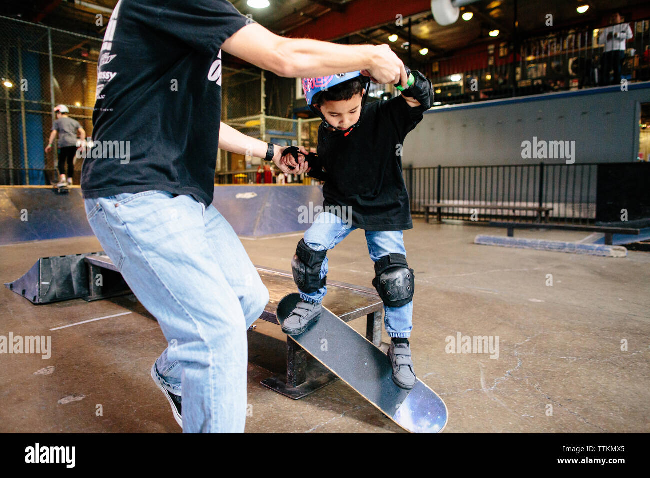 Young boy takes a jump with skateboard while holding teacher's hands Stock  Photo - Alamy