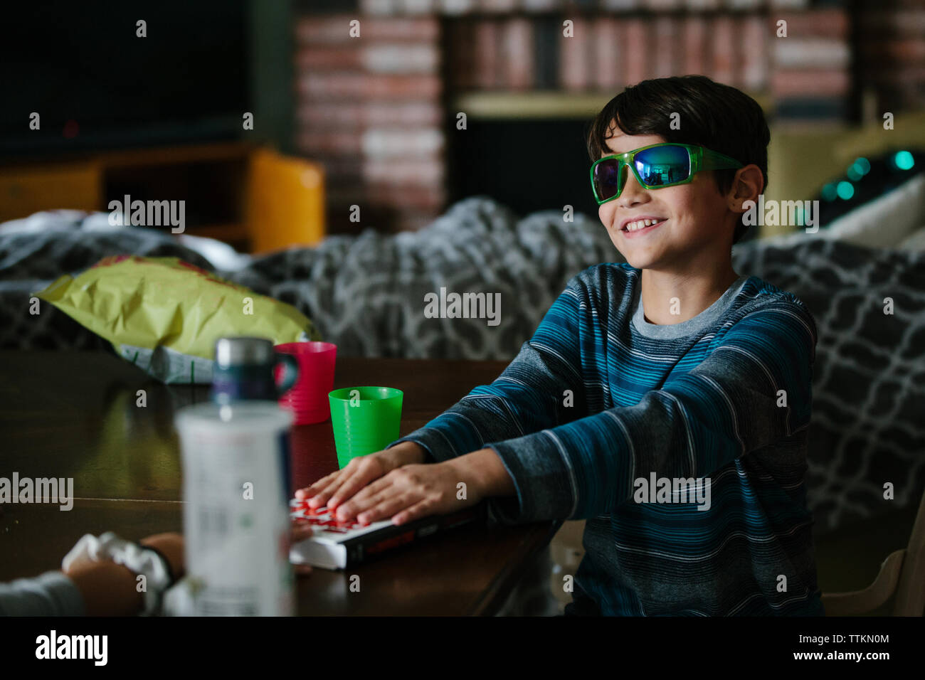 Boy wearing sunglasses inside smiles as he places hands on book Stock Photo